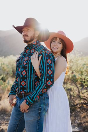A romantic desert photoshoot featuring a couple in western wear against mountain backdrop.