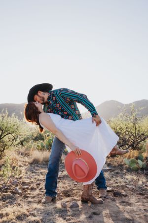 A romantic dip pose in desert setting with couple in western-inspired outfits.