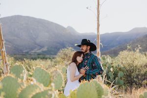 Romantic desert photoshoot with mountains and cactus in background at sunset.