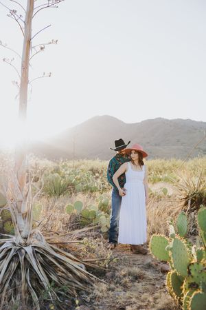 Desert engagement photos with couple among cactus and mountain backdrop.
