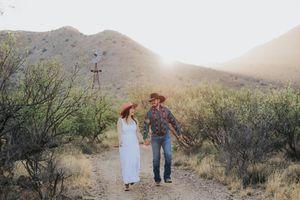 Couple walking hand in hand through desert landscape at sunset.