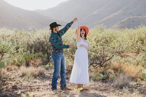 Couple dances playfully in desert setting with mountains and cacti.