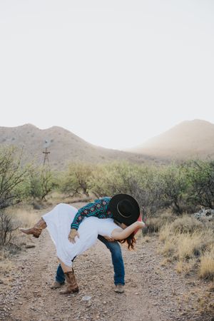 A playful dancing pose captured on a desert hiking trail with mountains in the background.