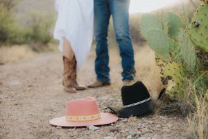 Two cowboy hats placed on a dusty trail with boots and desert scenery visible.