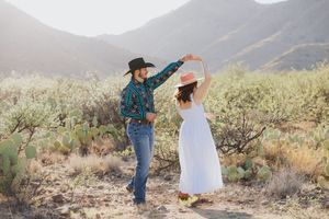 Two people share a romantic dance among desert plants with mountains in background.