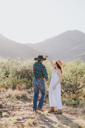 Couple explores desert landscape together with mountains and cacti in background.
