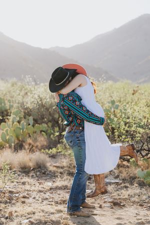 Couple shares romantic embrace surrounded by desert flora and mountain views.
