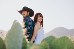 A couple shares a joyful moment in a desert setting with mountains in the background.