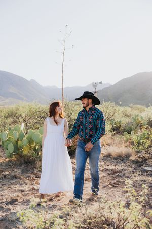 Two people share a romantic moment among desert plants and mountain views.
