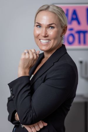 Professional in black blazer smiling confidently in office environment.