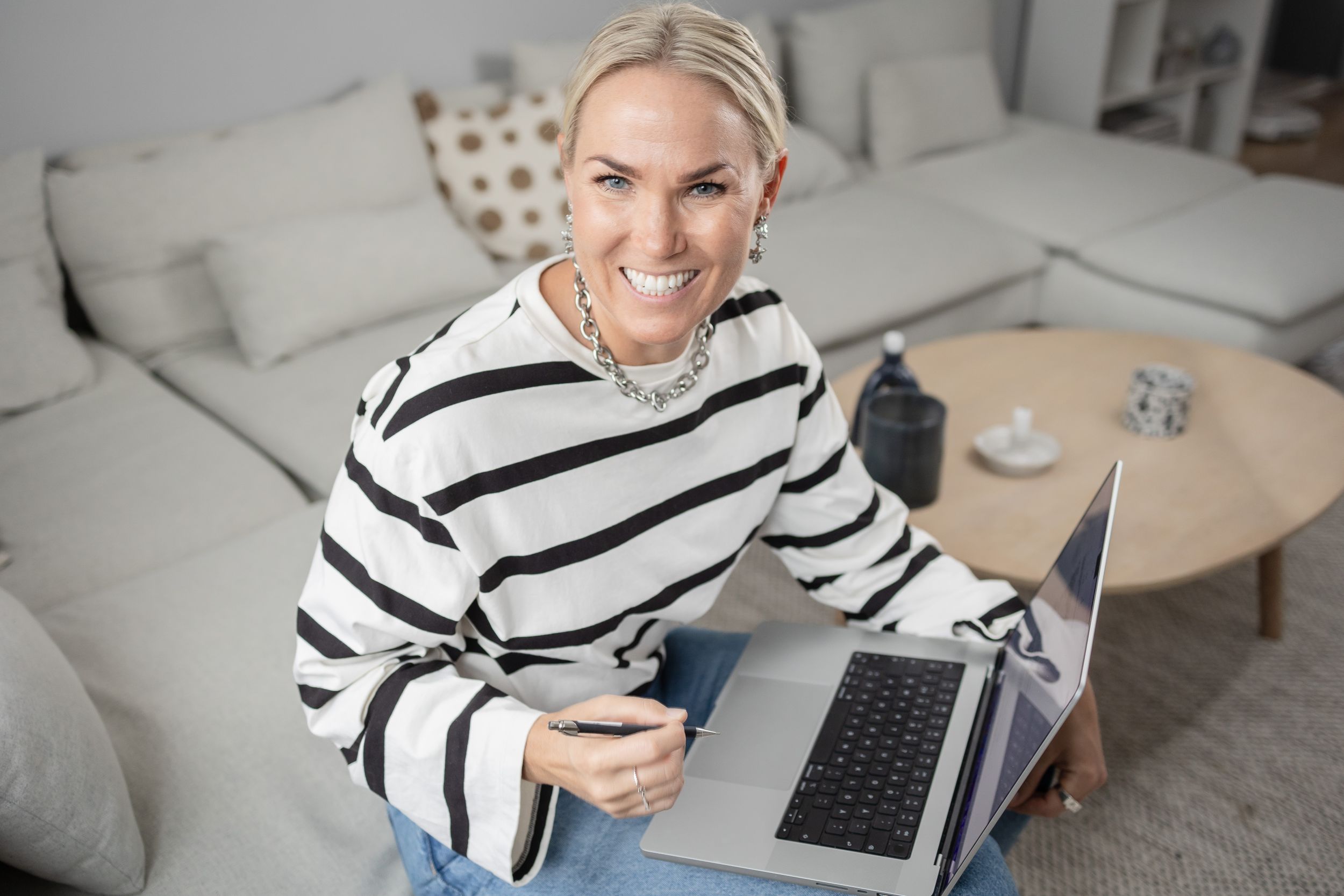 Professional working from home on laptop wearing striped sweater in cozy living room setting.