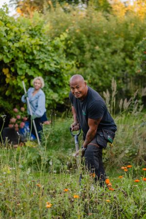 People gardening together in a lush outdoor garden with autumn foliage.