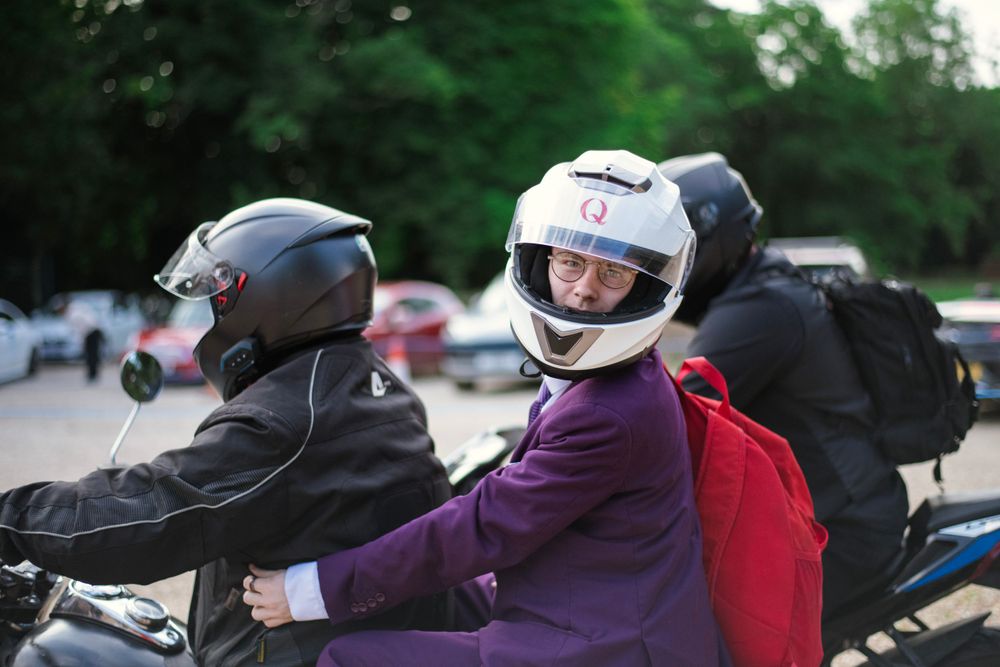 Two people wearing motorcycle helmets sit together on a parked motorcycle.