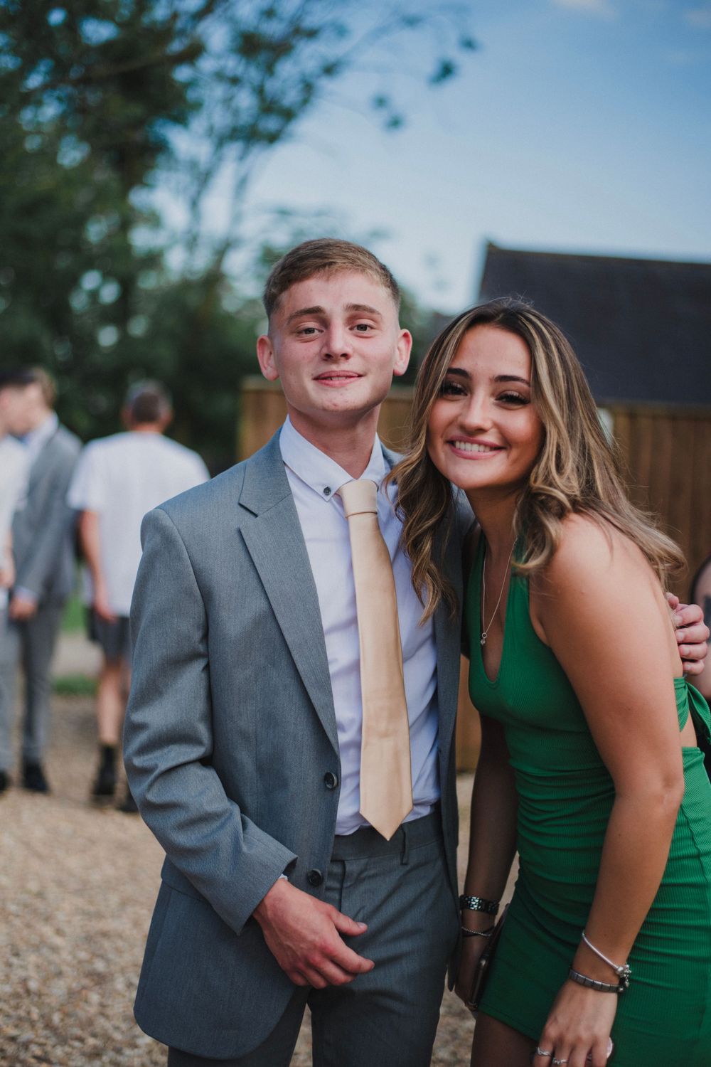 Two elegantly dressed guests pose together at an outdoor event, with the woman wearing a green dress.