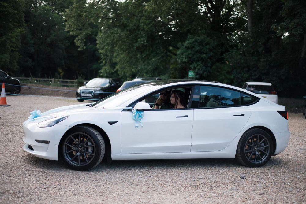 A white Tesla Model 3 with black wheels parked in a wooded area.