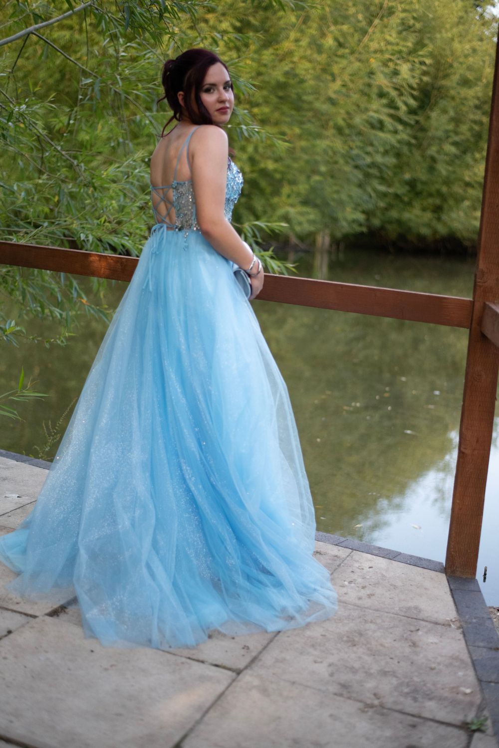 A flowing light blue tulle gown photographed from behind near a reflecting pond.