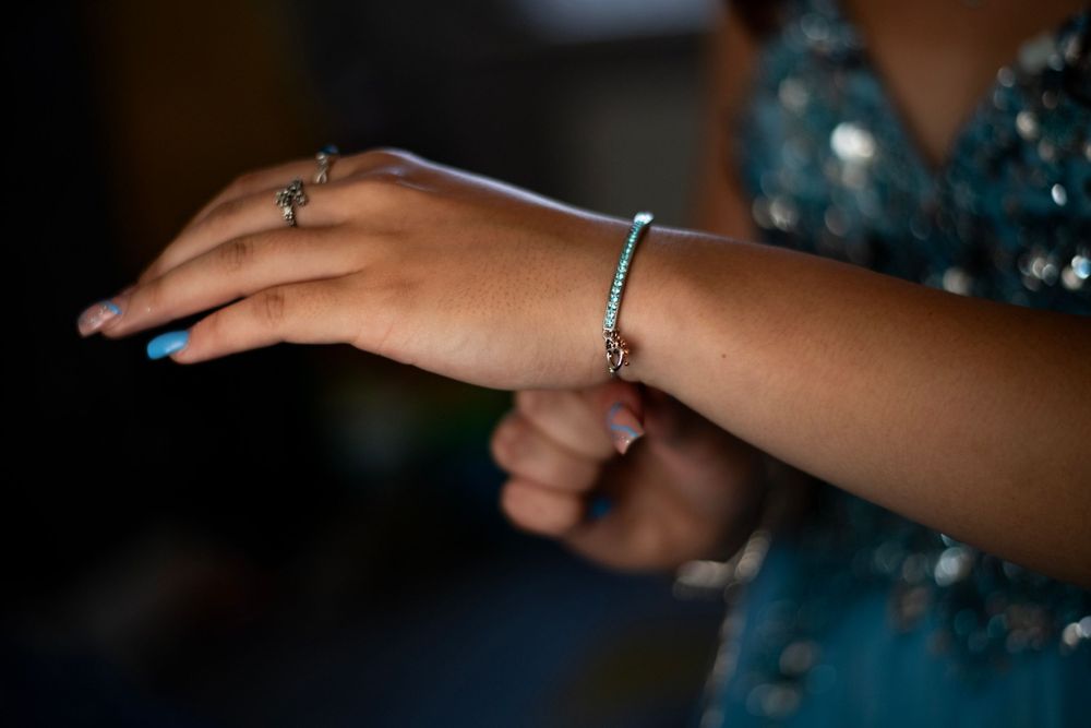 Close-up of bracelet and ring with blue manicured nails.