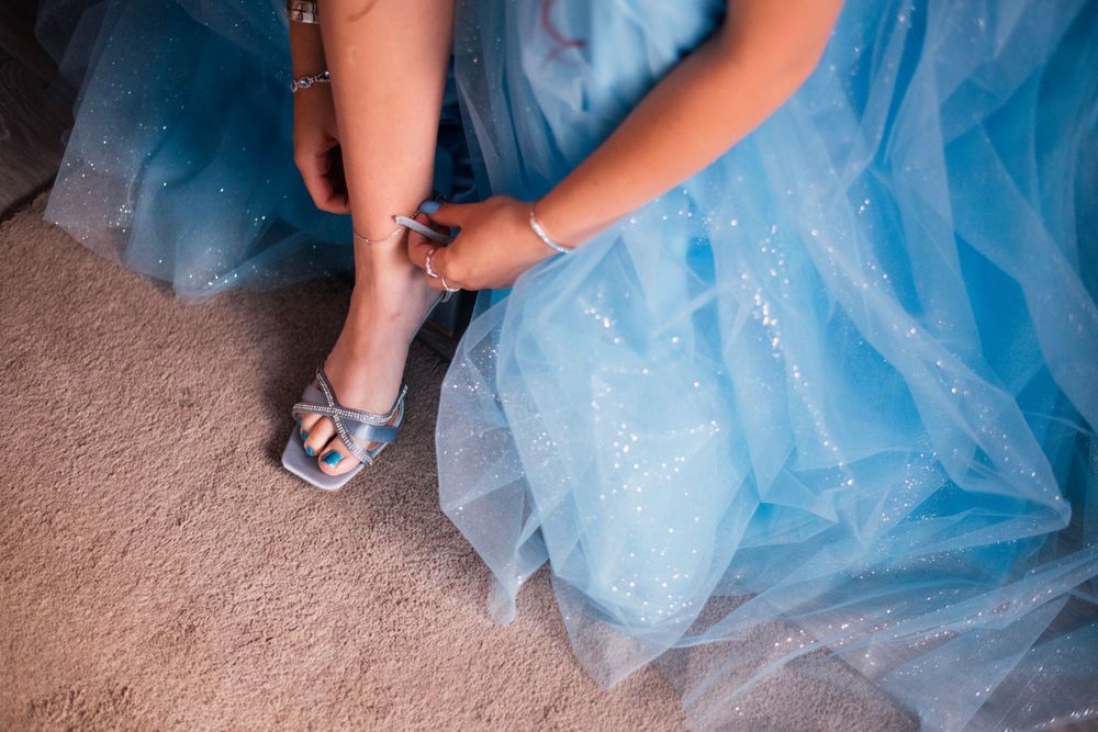 Person putting on silver heels while wearing light blue tulle dress.