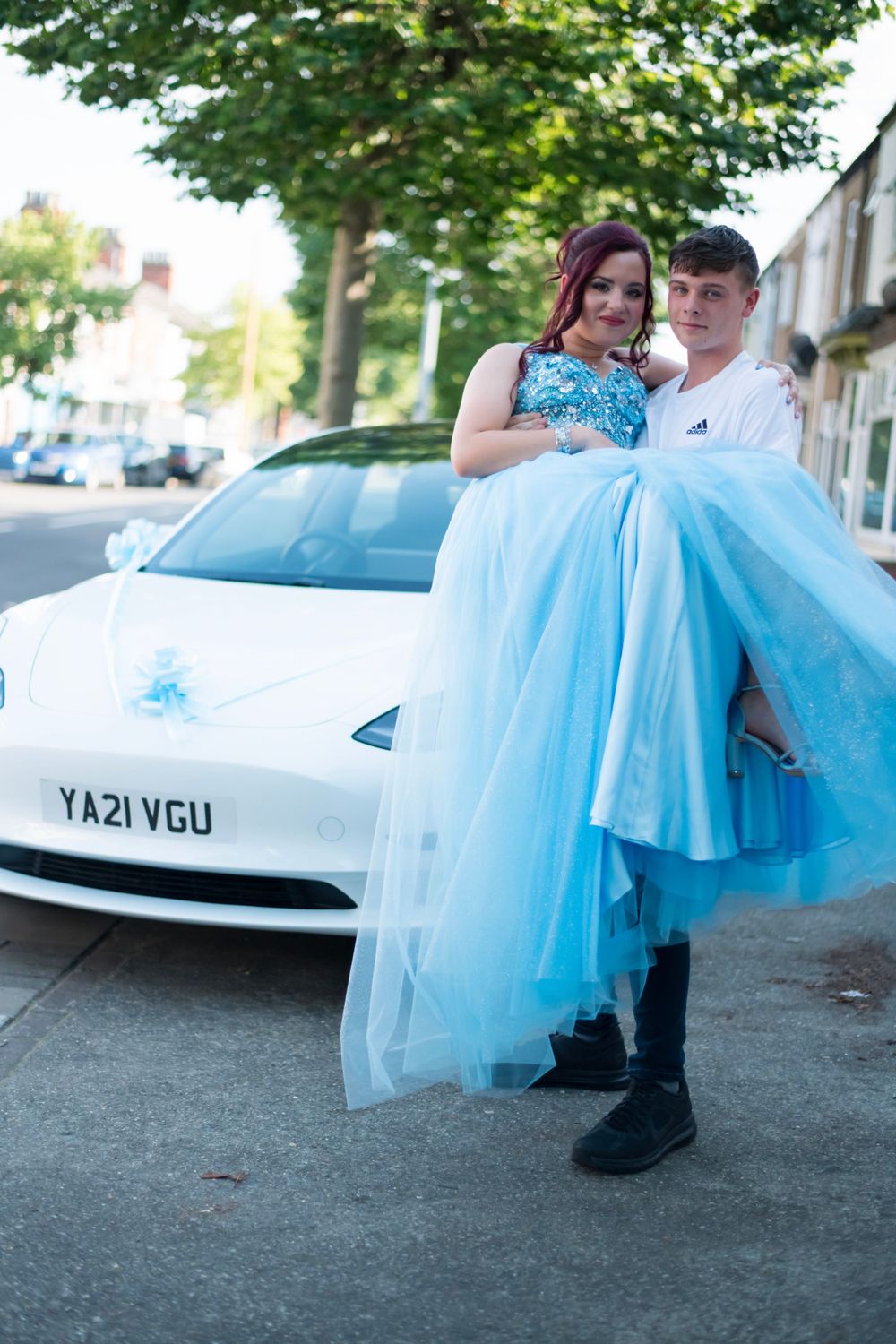 A couple poses with a white Tesla decorated for a special occasion.