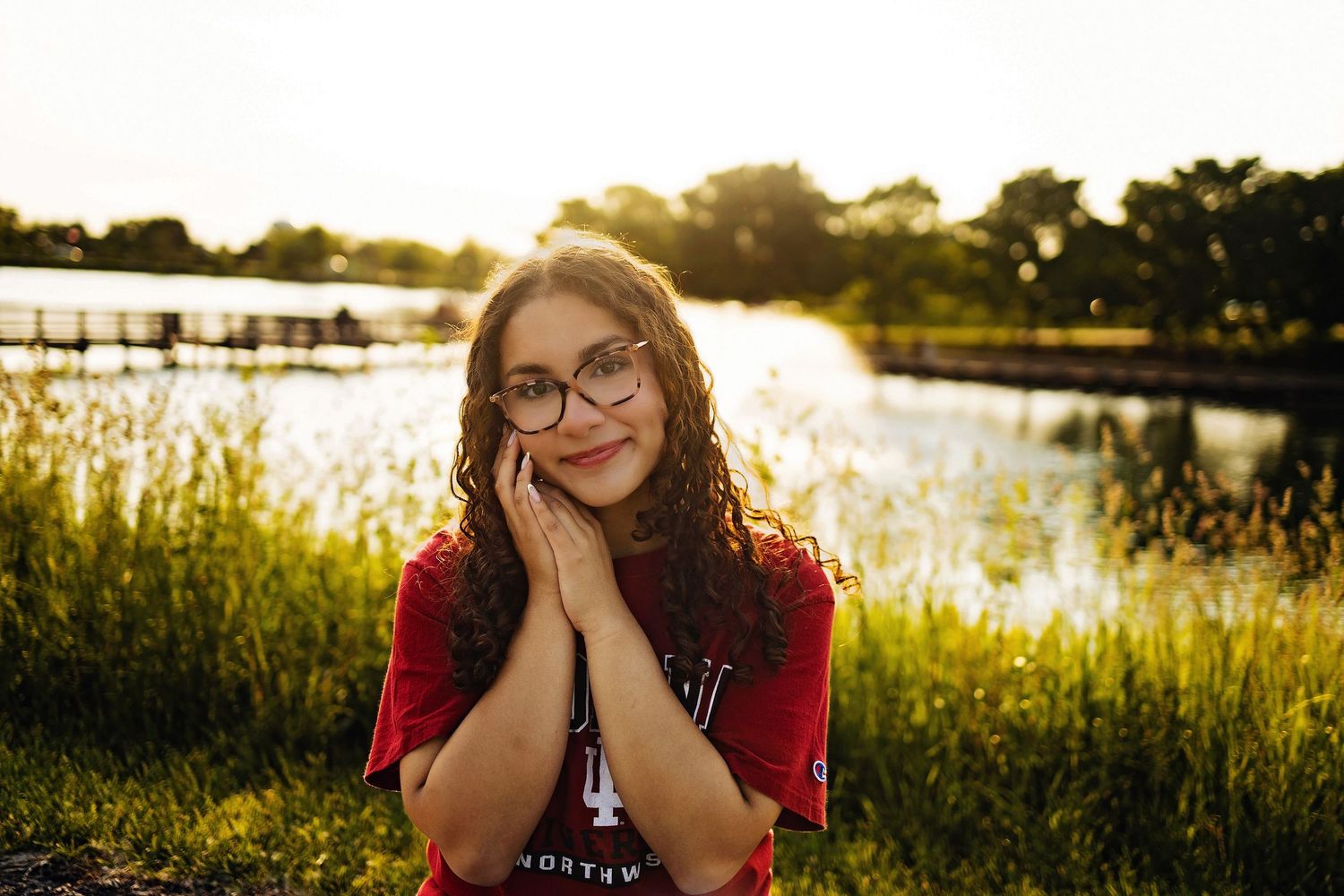 Portrait at sunset by a lake with golden sunlight filtering through trees in the background.
