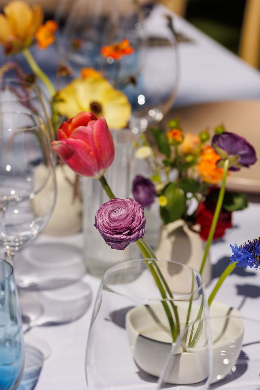 Colorful spring flowers in elegant glass vases on a white tablecloth for a festive table setting.