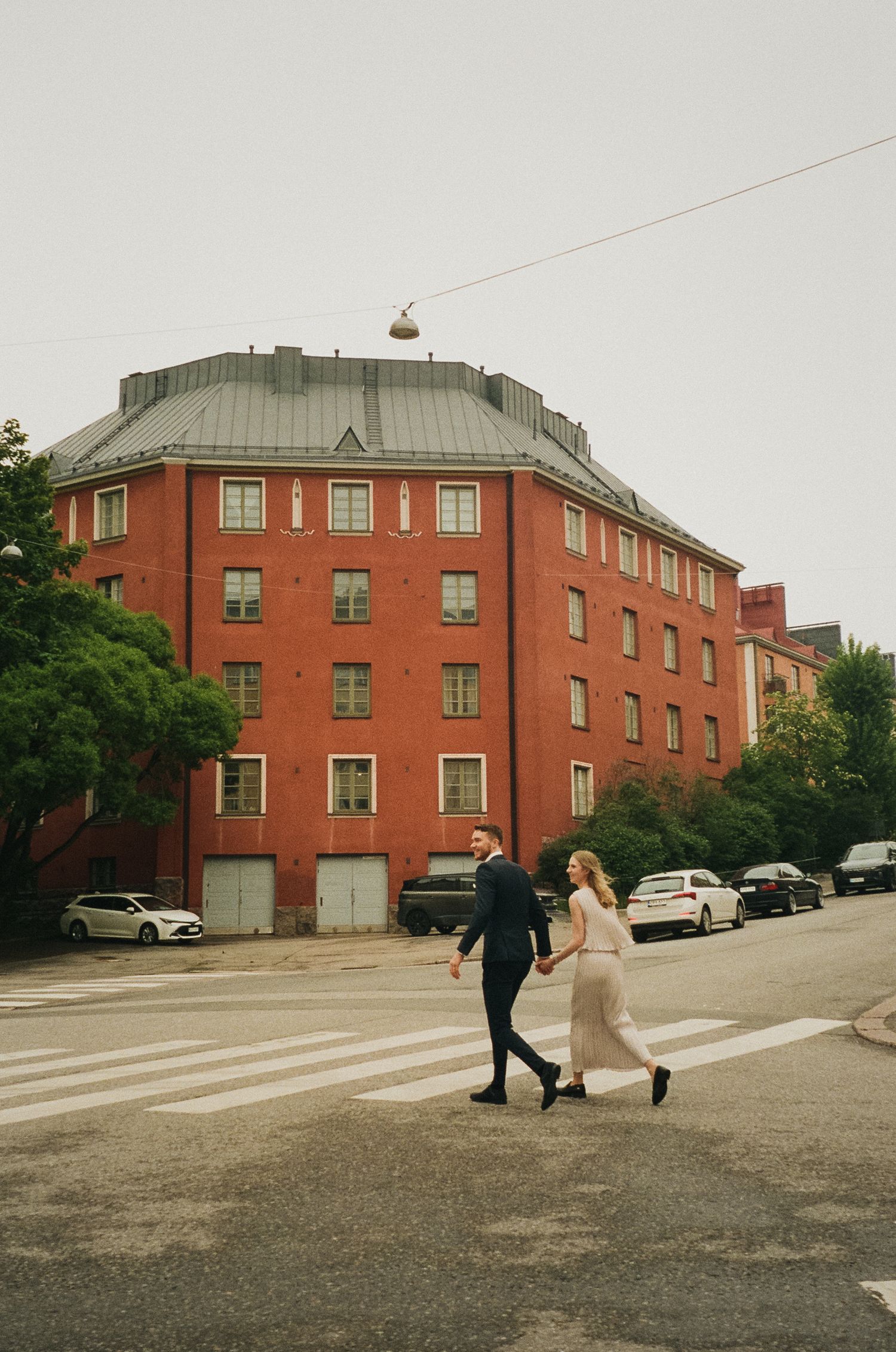 Couple walking near red brick building on overcast day.