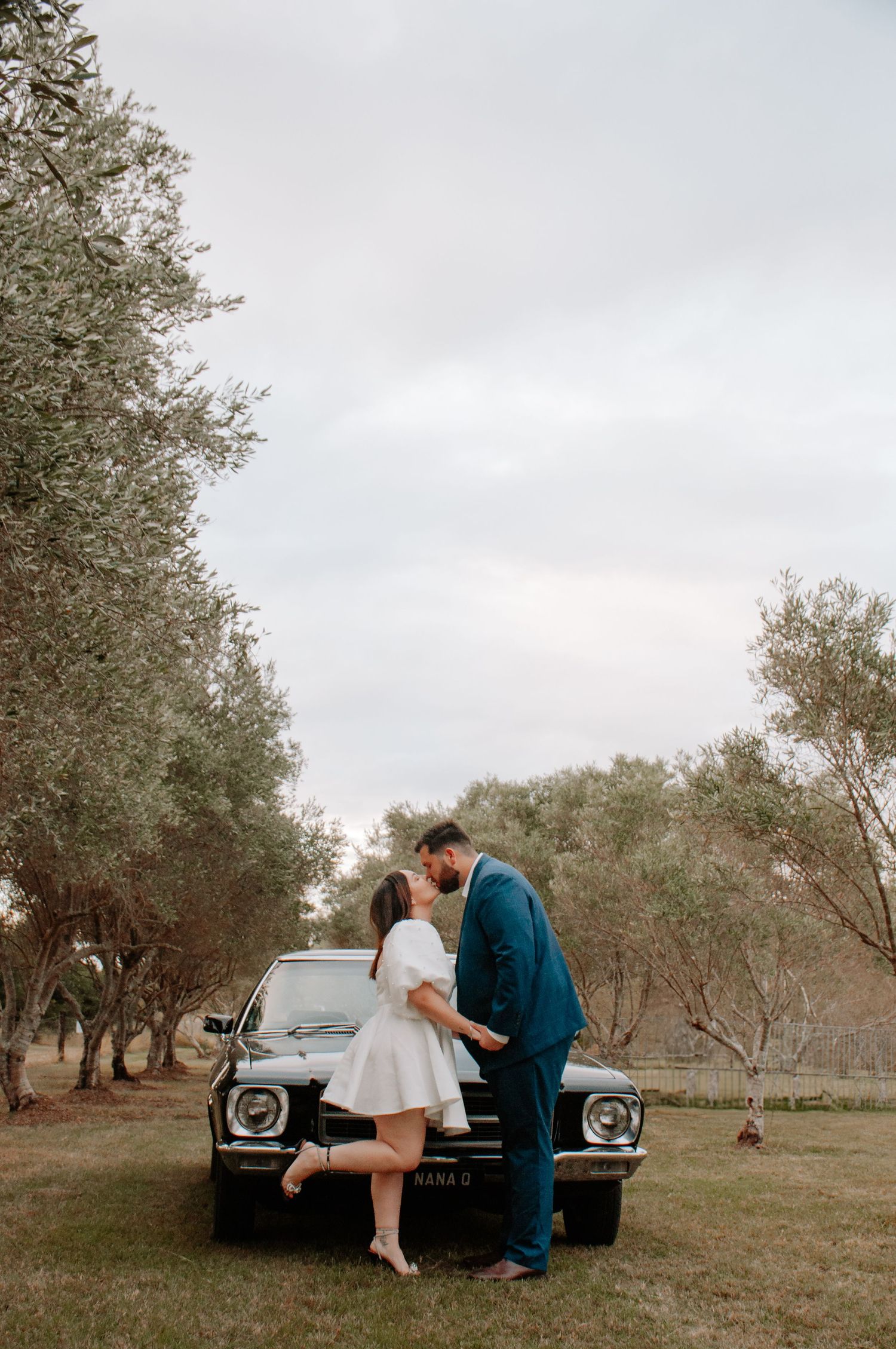 couple kissing in front of an old car at an olive farm. engagement photo session