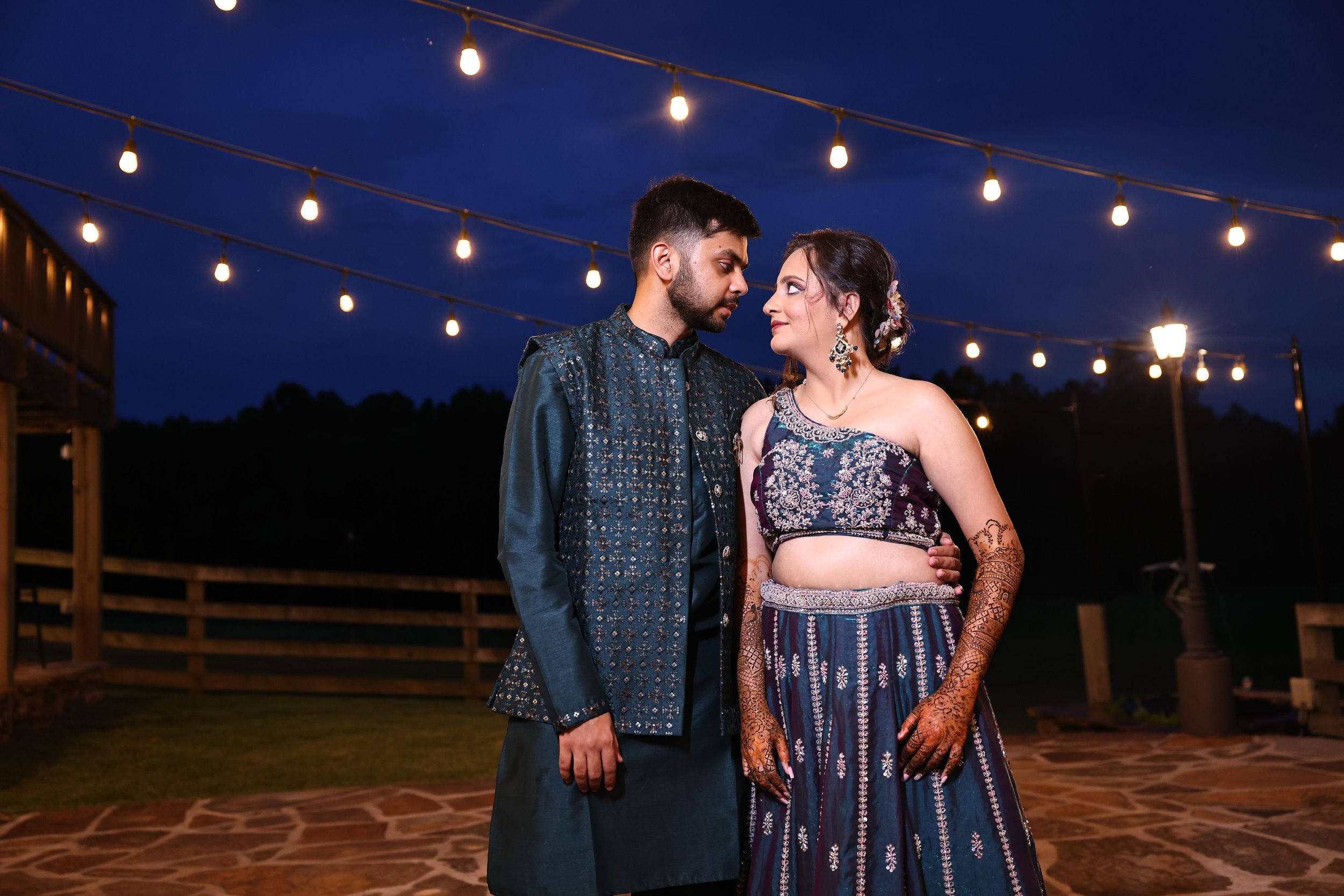 Bride and groom share a romantic wedding portrait under outdoor string lights, capturing an intimate evening celebration.