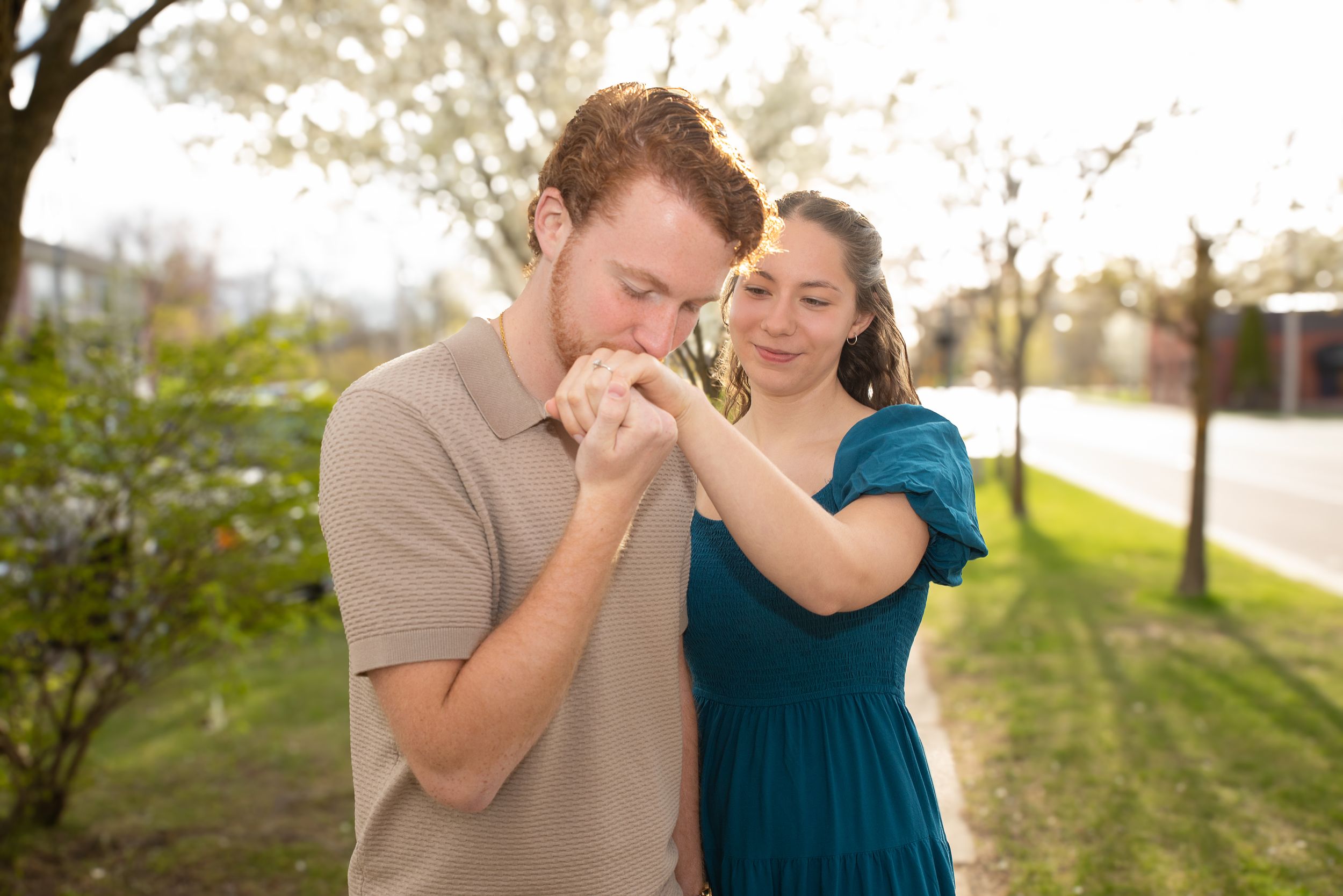 A couple stands together in a sunlit garden setting, holding hands in a romantic spring moment.