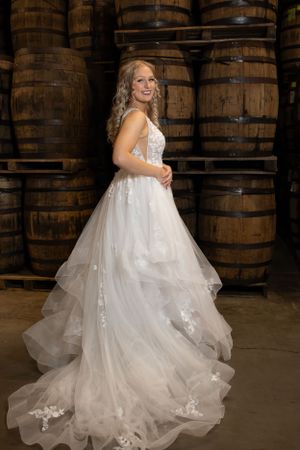 An elegant wedding dress displayed in a rustic barrel room setting.