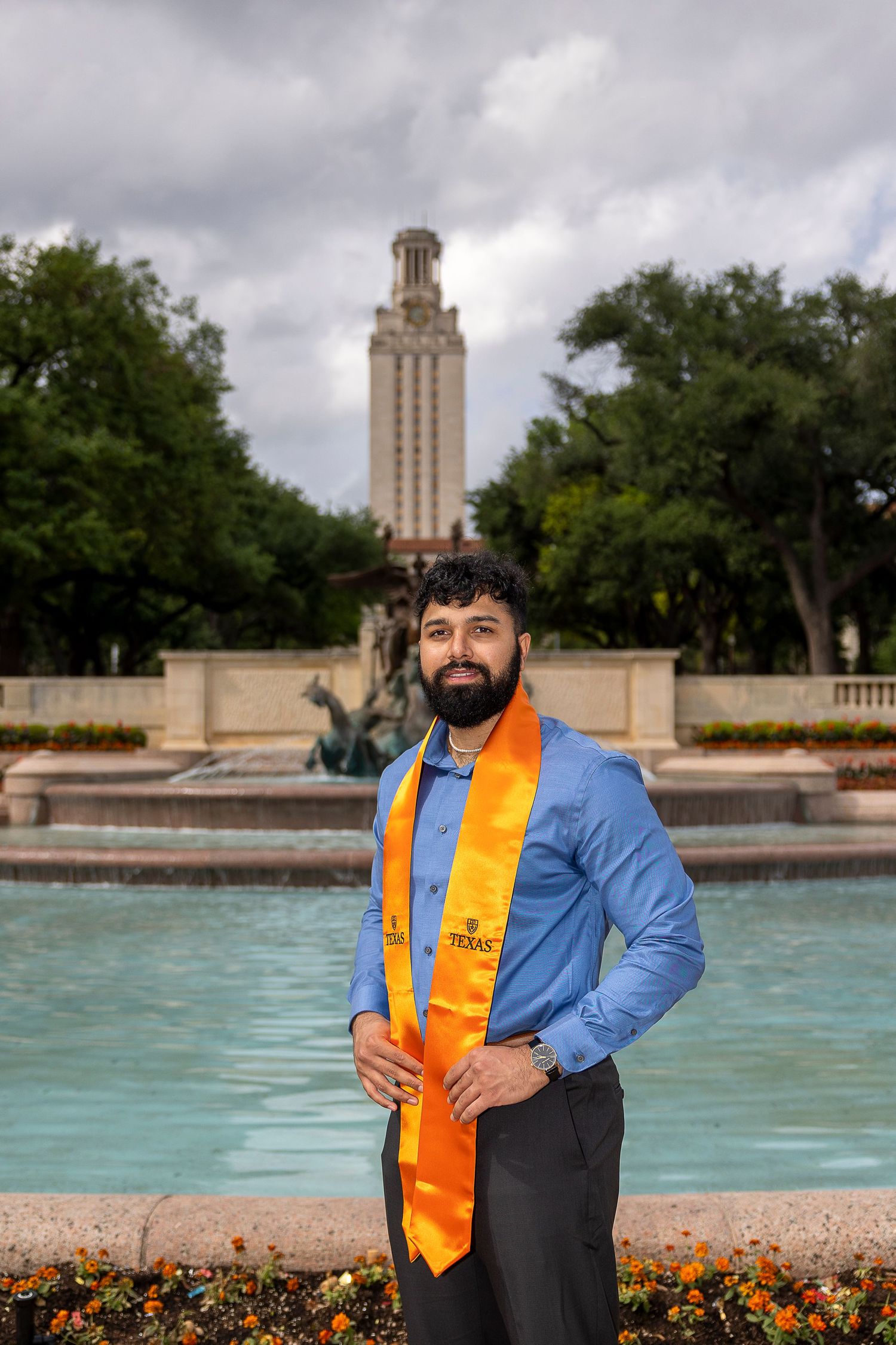 Graduation portraits taken at the University of Texas Tower with turquoise reflecting pool and orange flowers in foreground.
