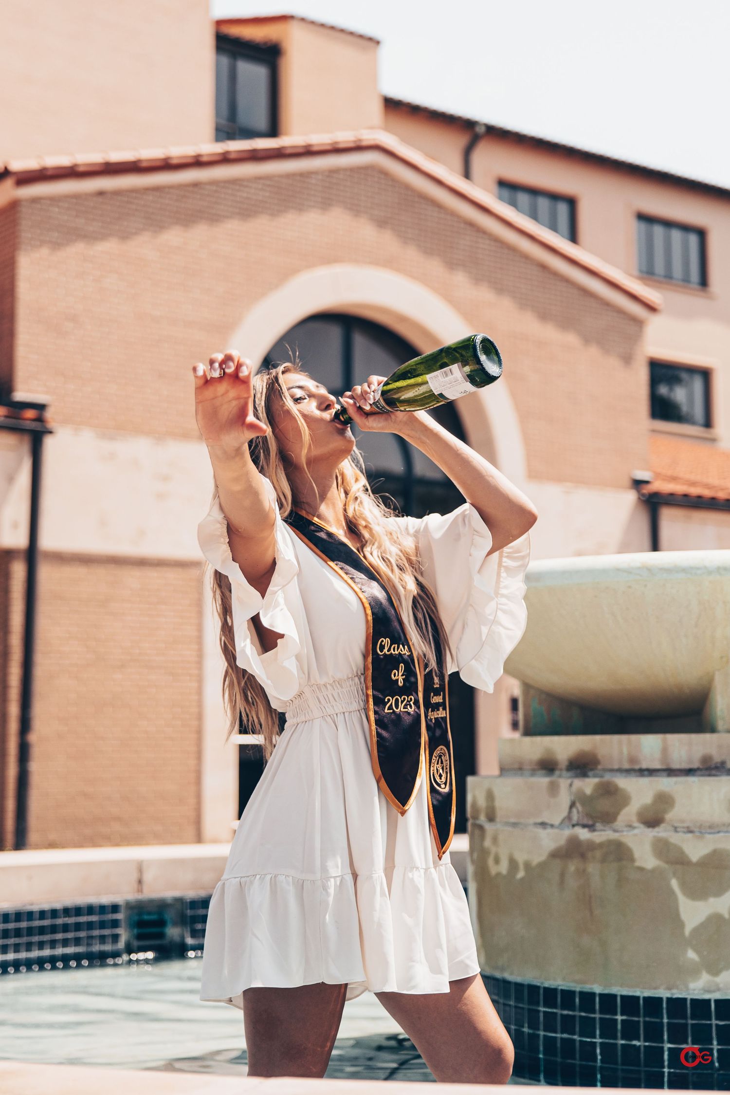 Four women in white dresses drinking from bottles while enjoying a sunny day by the pool.