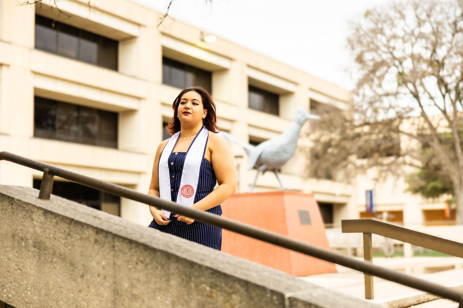 A person in a navy blue outfit poses on concrete steps in front of a building.