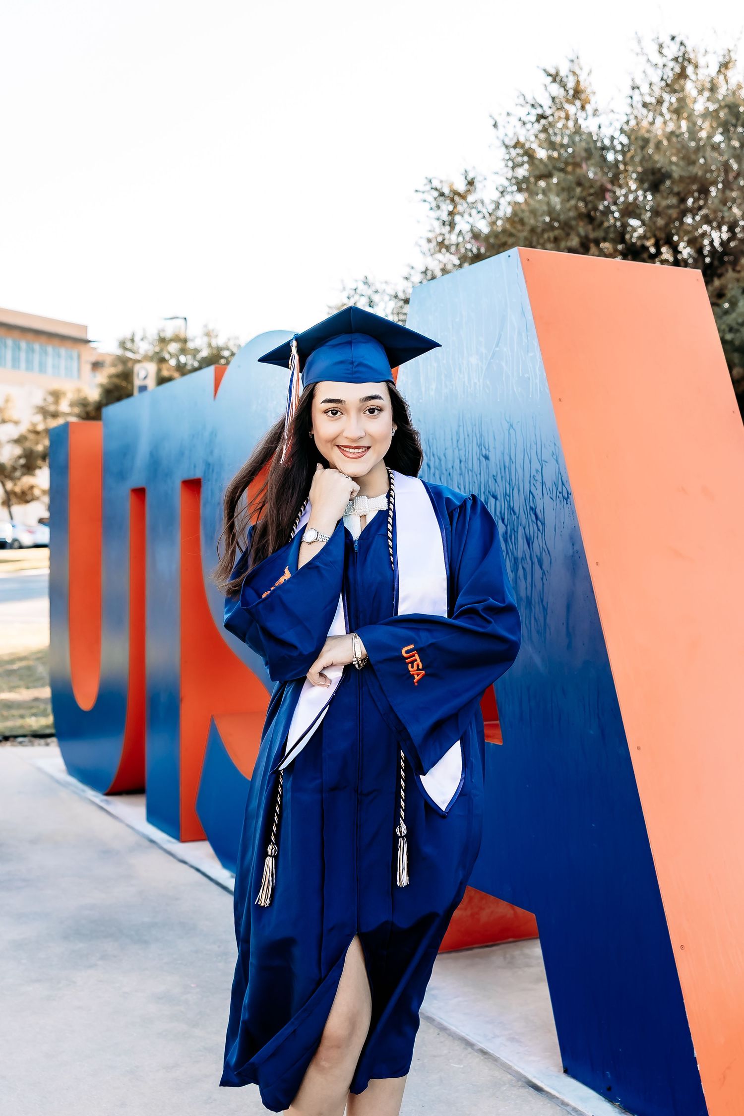 Graduate in blue cap and gown poses for photos in front of orange and blue architectural wall installation.