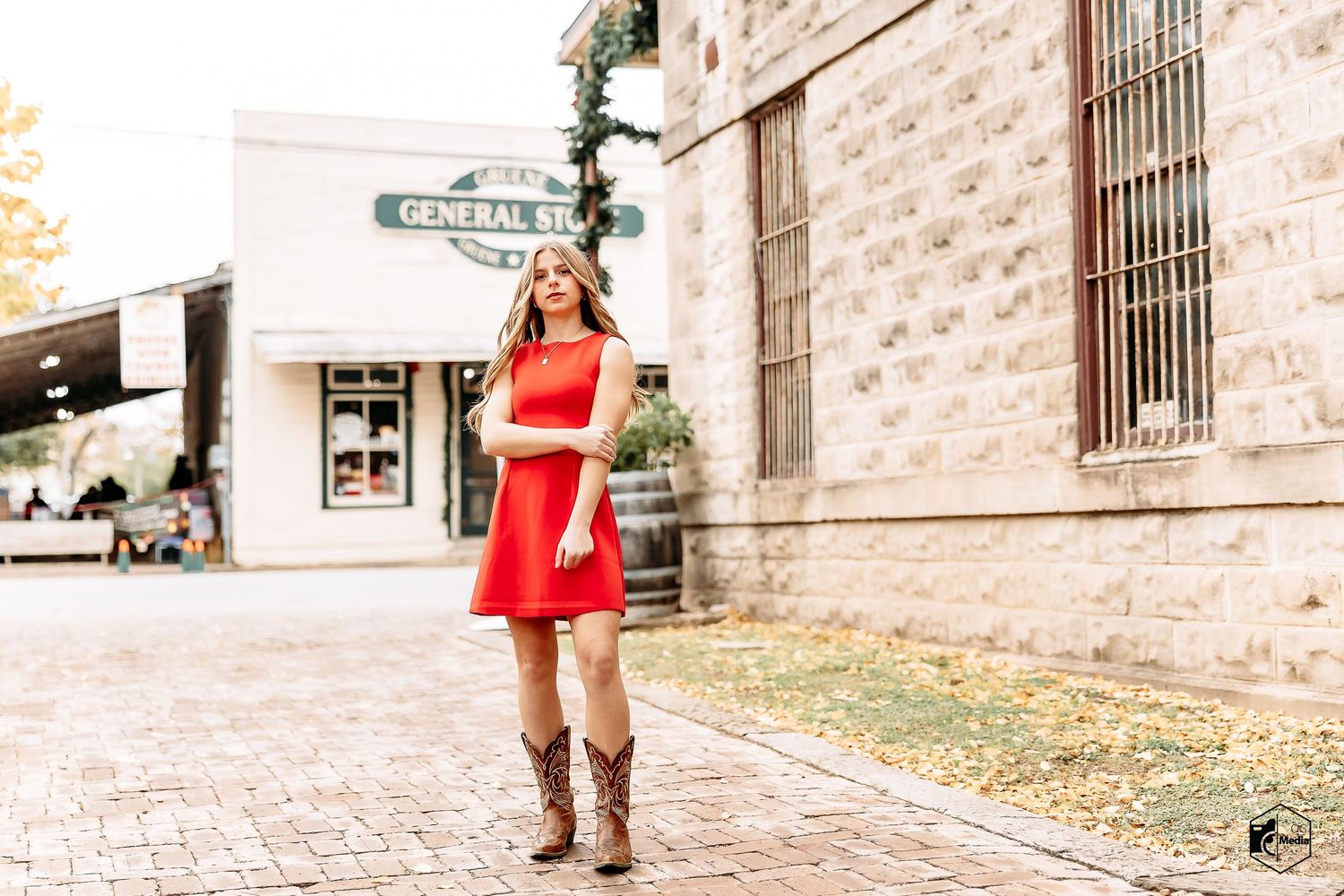 A person in a red sweater walks down a cobblestone street near historic brick buildings on a sunny day.