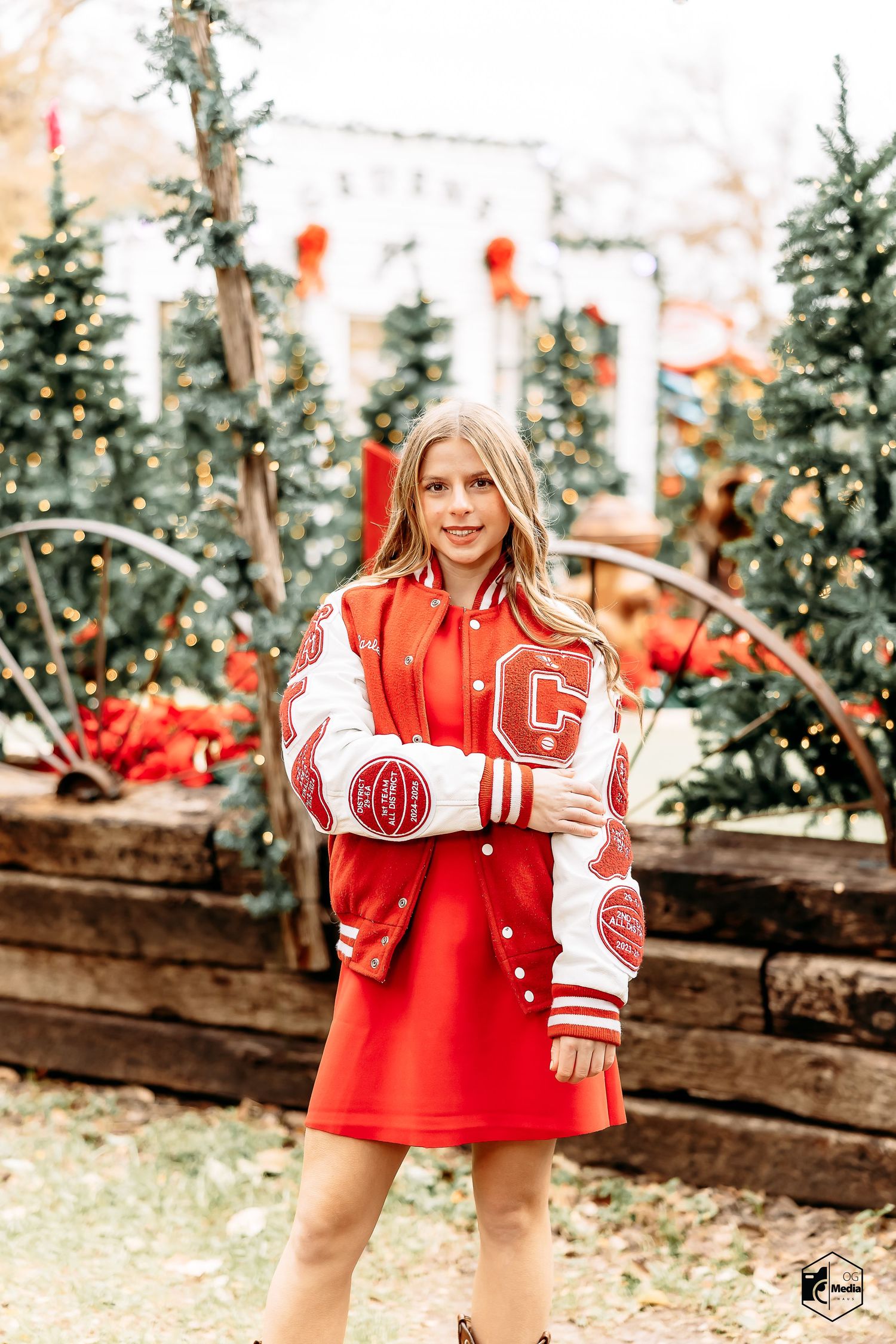 Red and white varsity letterman jacket styled with a red dress against evergreen trees and holiday decorations.
