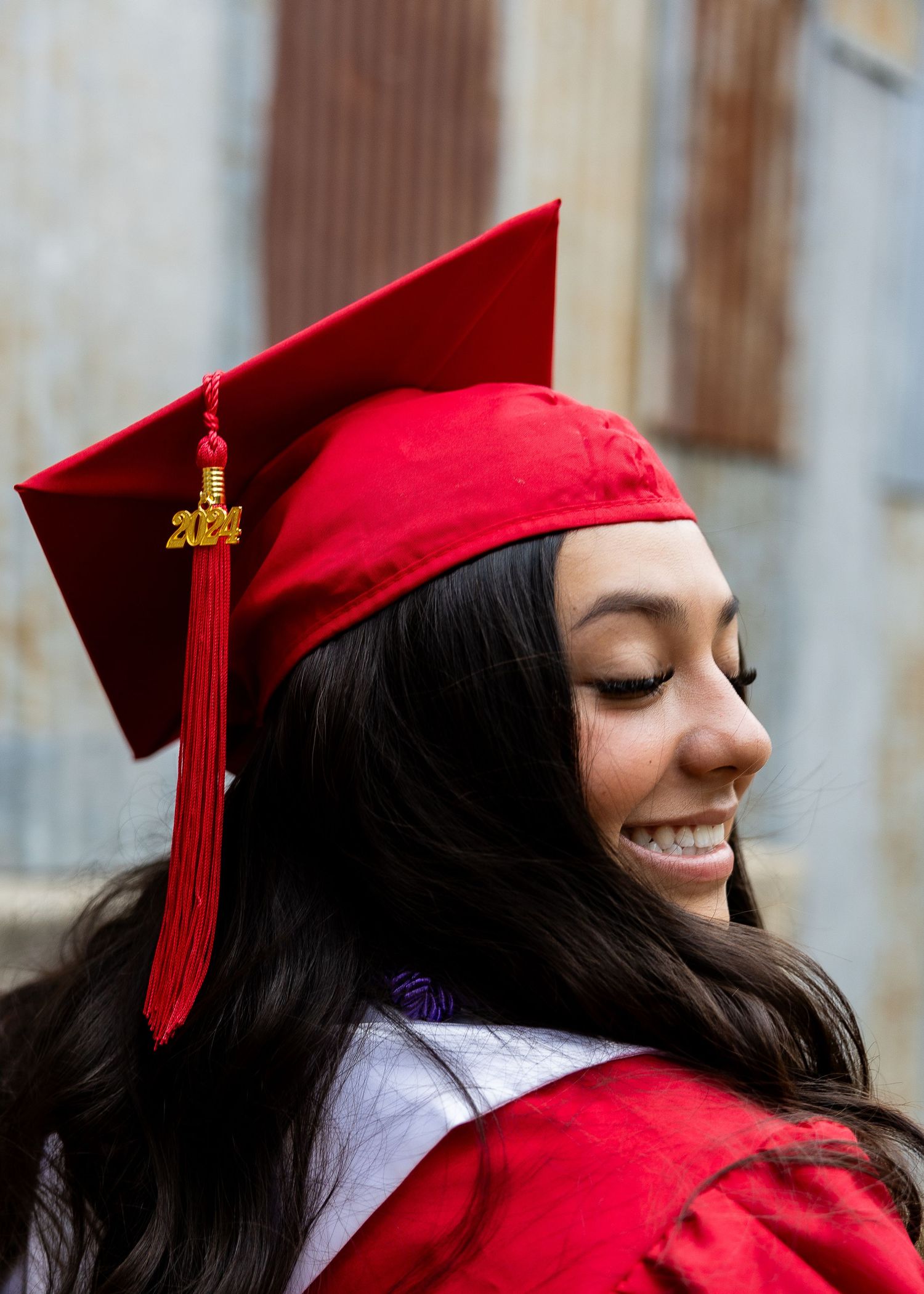 A graduate in a red cap and gown smiles brightly during a graduation photo session.