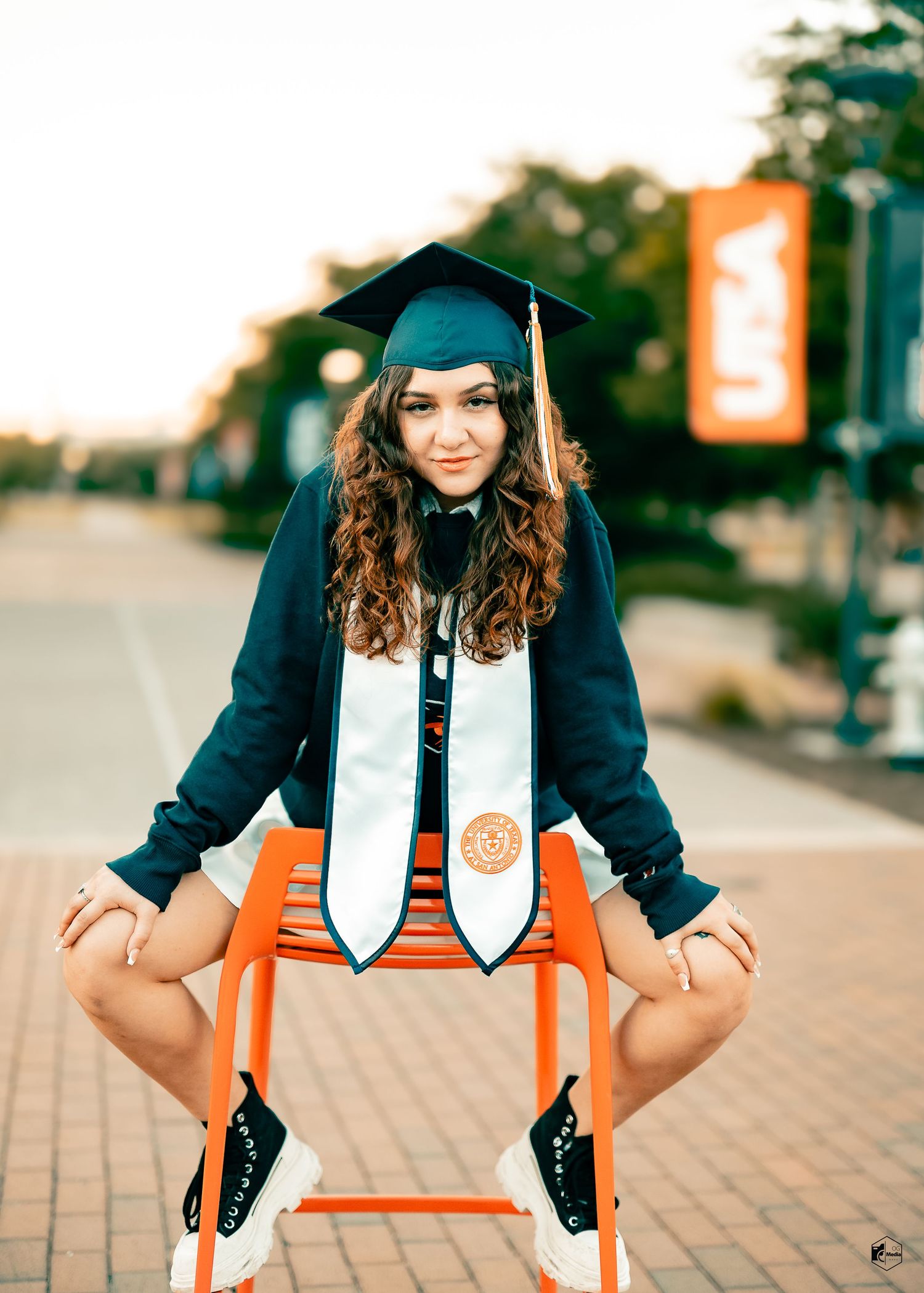 Graduate in cap and gown poses on brick walkway with orange and white graduation stoles in series of photos.