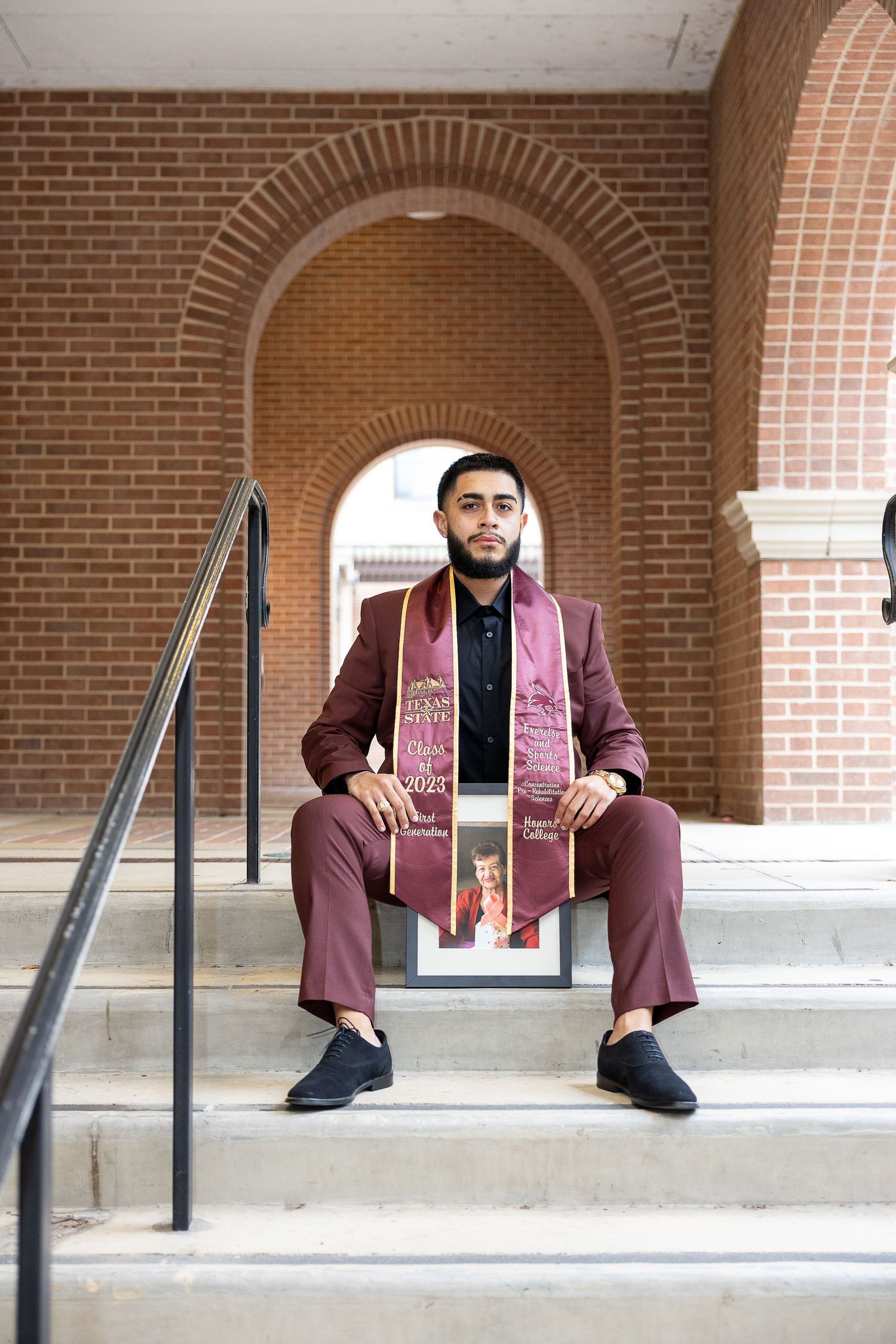 A person in a burgundy suit sits under brick archways in a creative portrait series.
