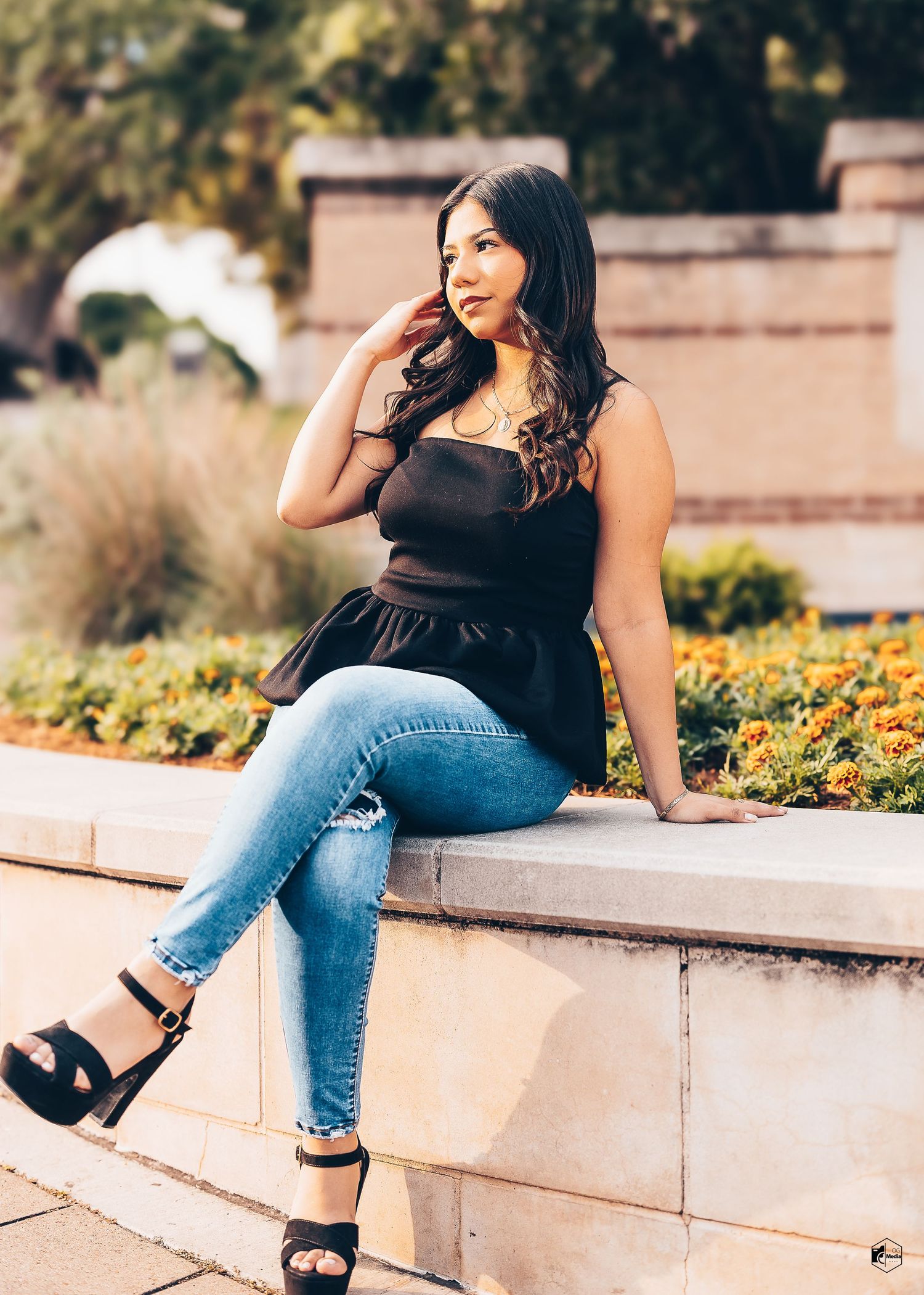Stylish outfit featuring black peplum top paired with distressed jeans and platform sandals in a garden setting.