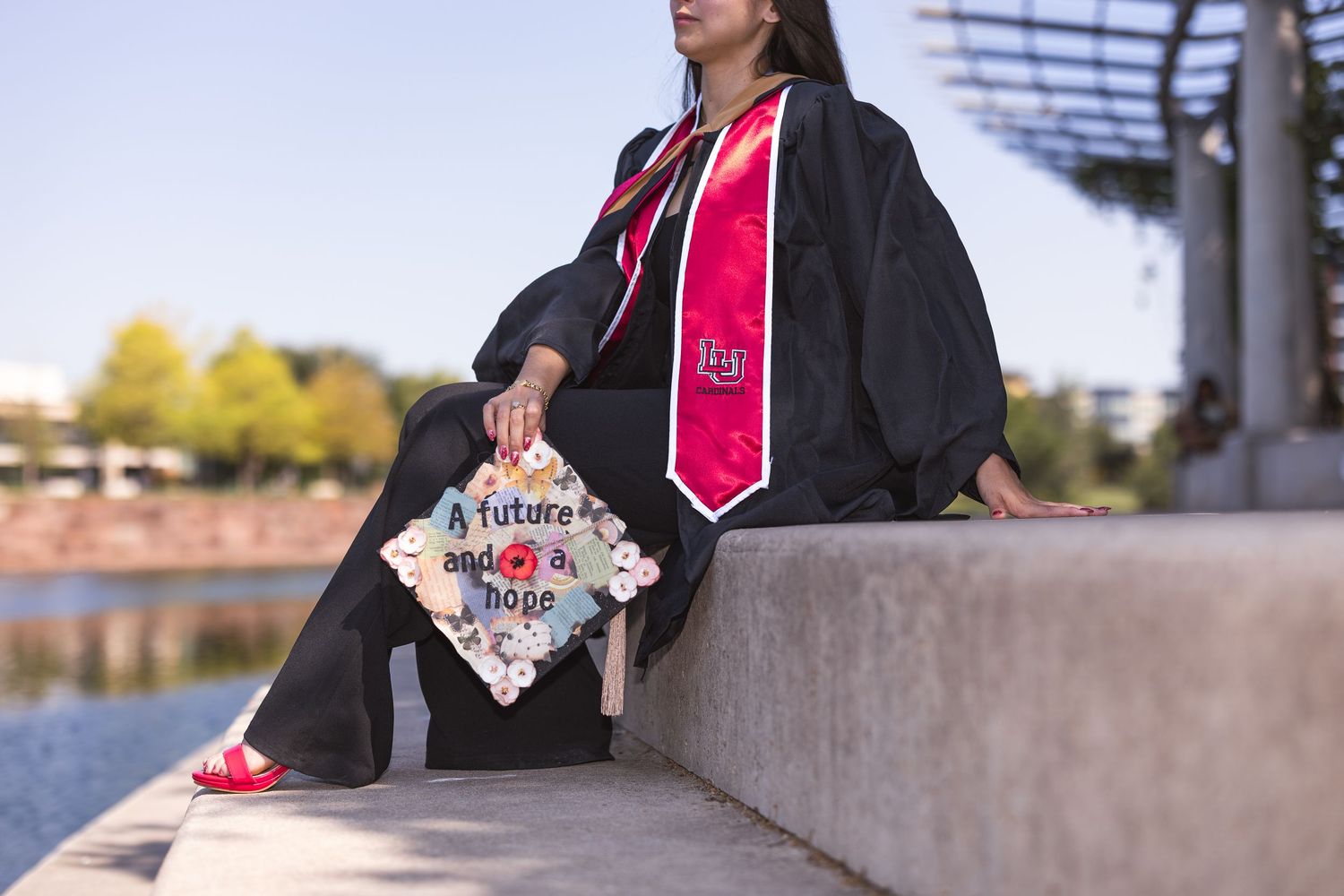 A group of graduates in black caps and gowns with pink stoles stand together in an outdoor setting.