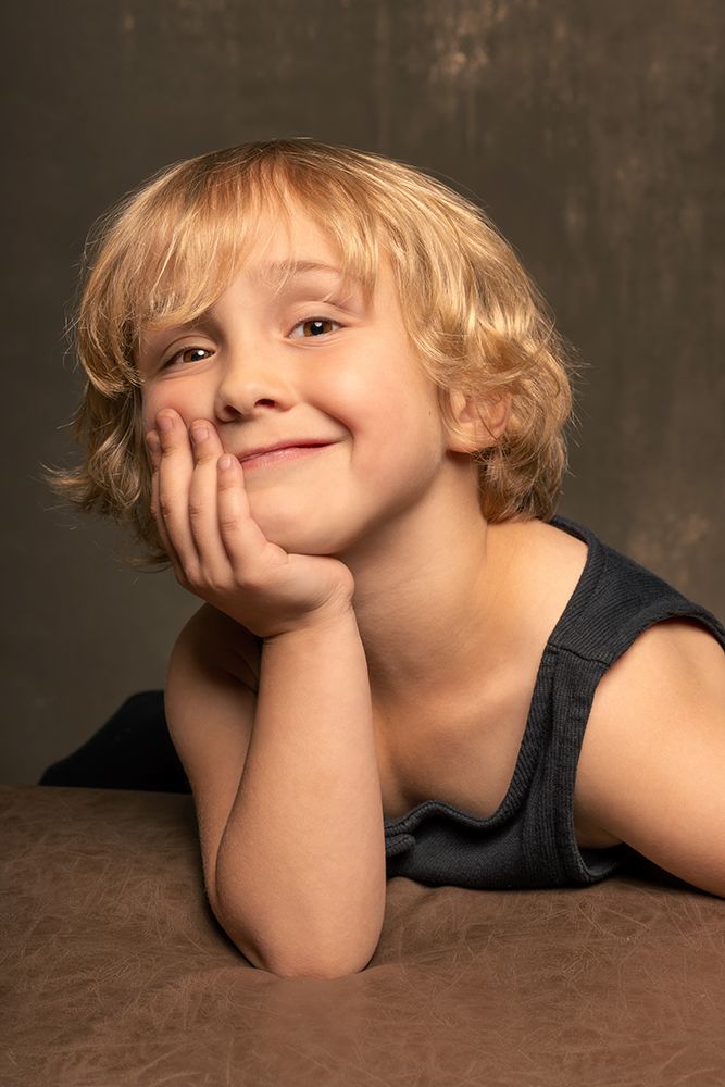Young person with blonde hair resting head on hand while lying down with a cheerful expression.