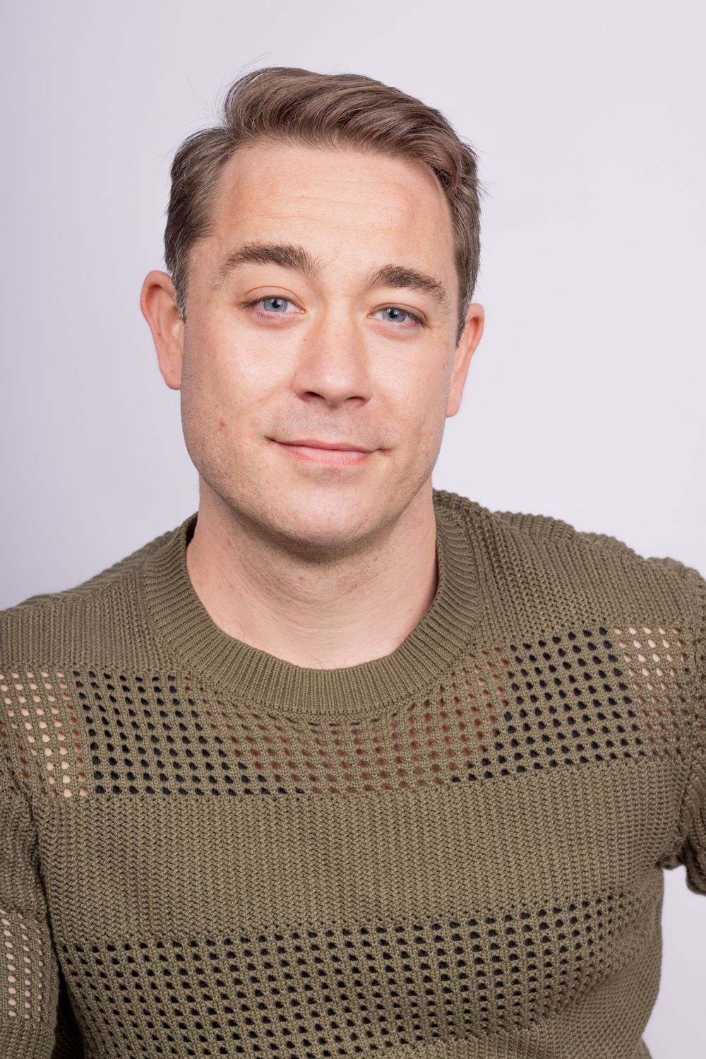 Professional headshot of person wearing olive green mesh sweater against light background.