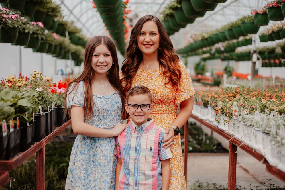 Mother with daughter and son posing together in a colorful greenhouse filled with blooming flowers.