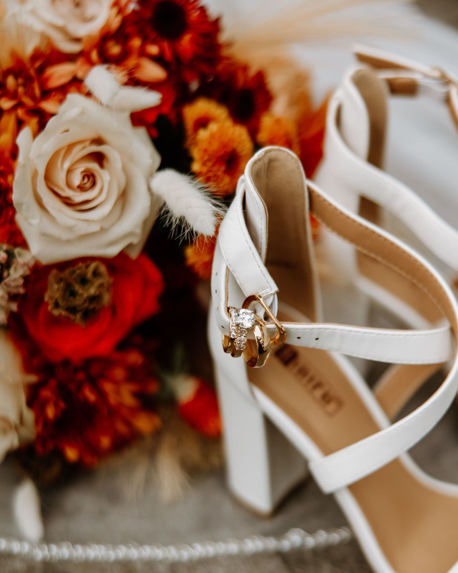 White bridal heels with diamond ring resting against vibrant red and orange fall wedding bouquet.