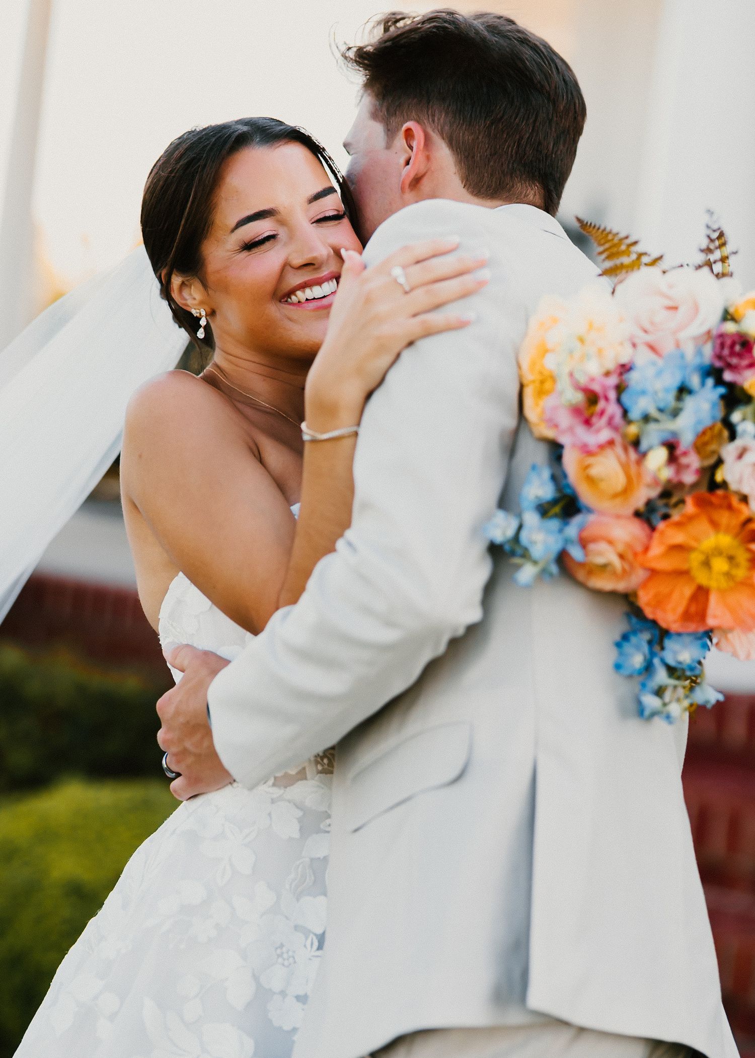 Joyful bride hugs groom holding colorful bouquet of orange blue and pink flowers.