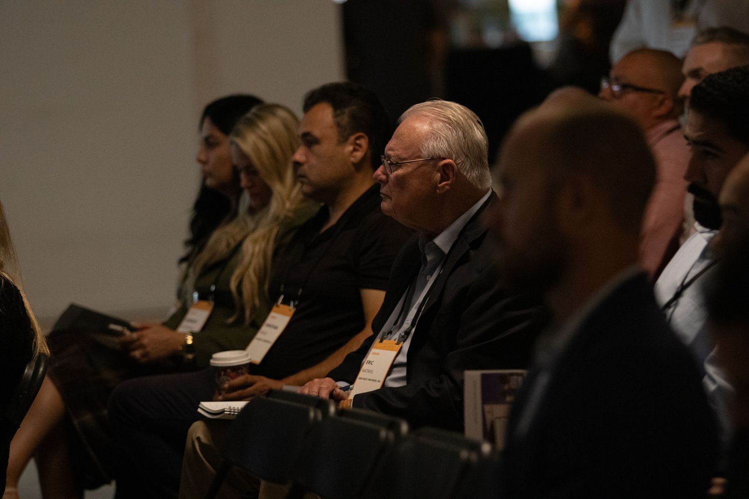 Audience members seated in rows at a professional conference or business event, listening attentively to a presentation.