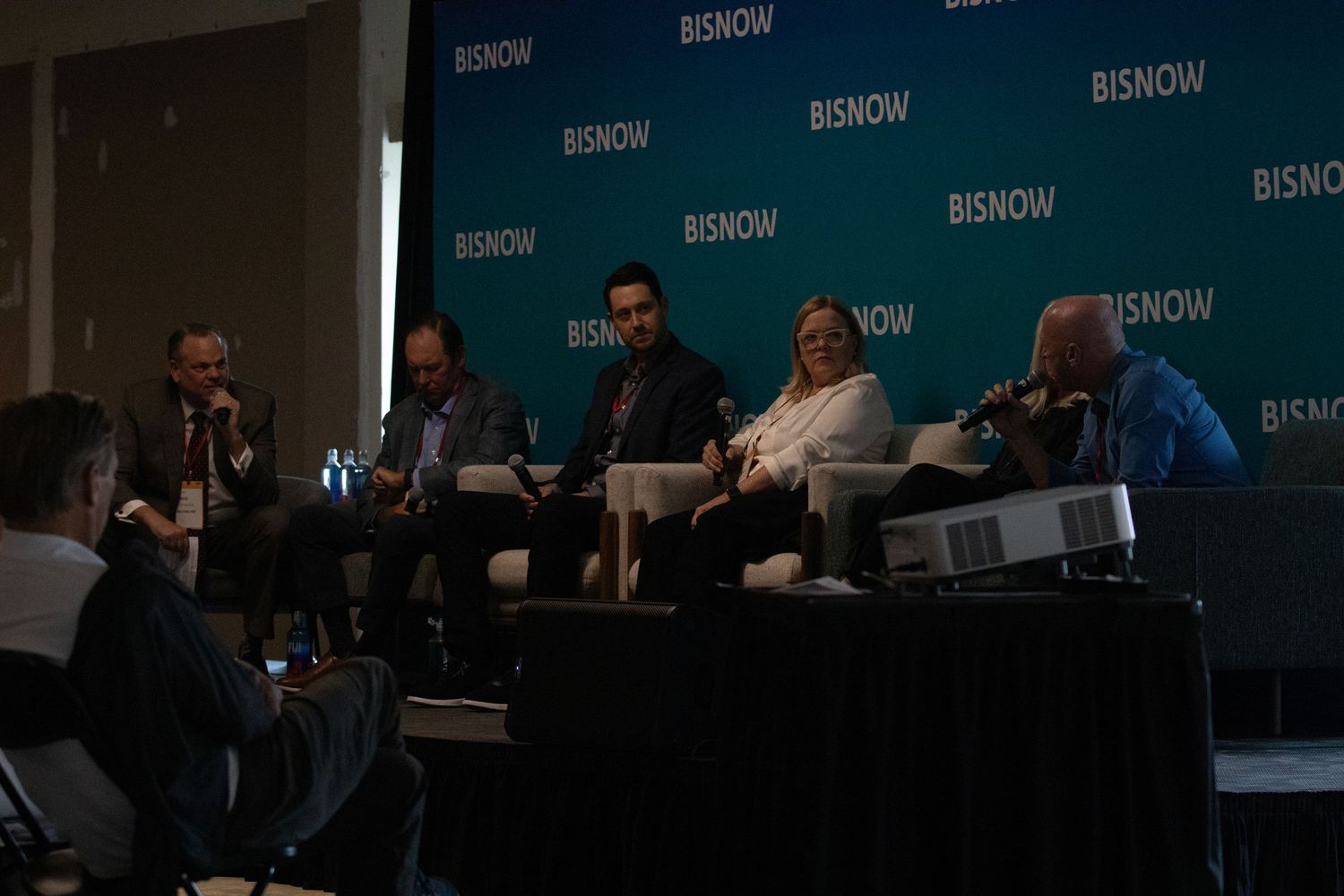 Panel of five speakers at a Bisnow commercial real estate conference seated on stage during a discussion.