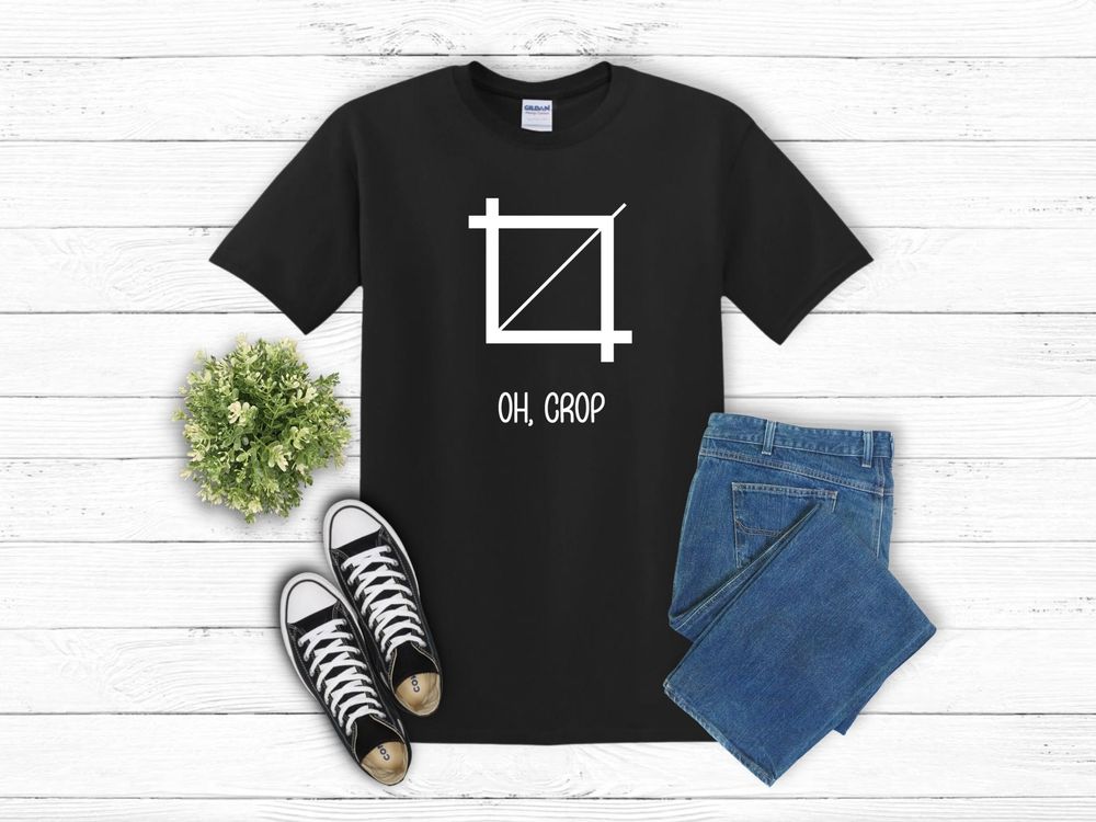 Flatlay of black t-shirt with crop icon design, paired with blue jeans, black sneakers and small green plant decoration.