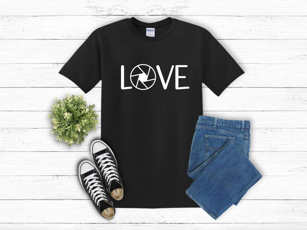 Black t-shirt with LOVE text featuring camera lens symbol, styled with blue jeans and black sneakers on white surface.